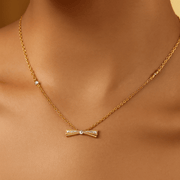 Gold bow-shaped necklace on a person's neck with a neutral background